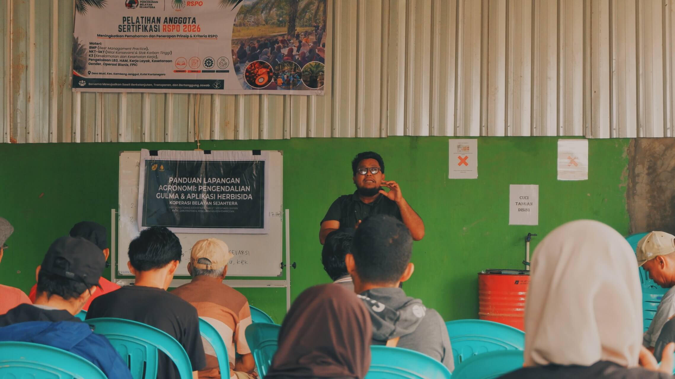 An instructor leads a classroom session while participants listen from turquoise chairs.