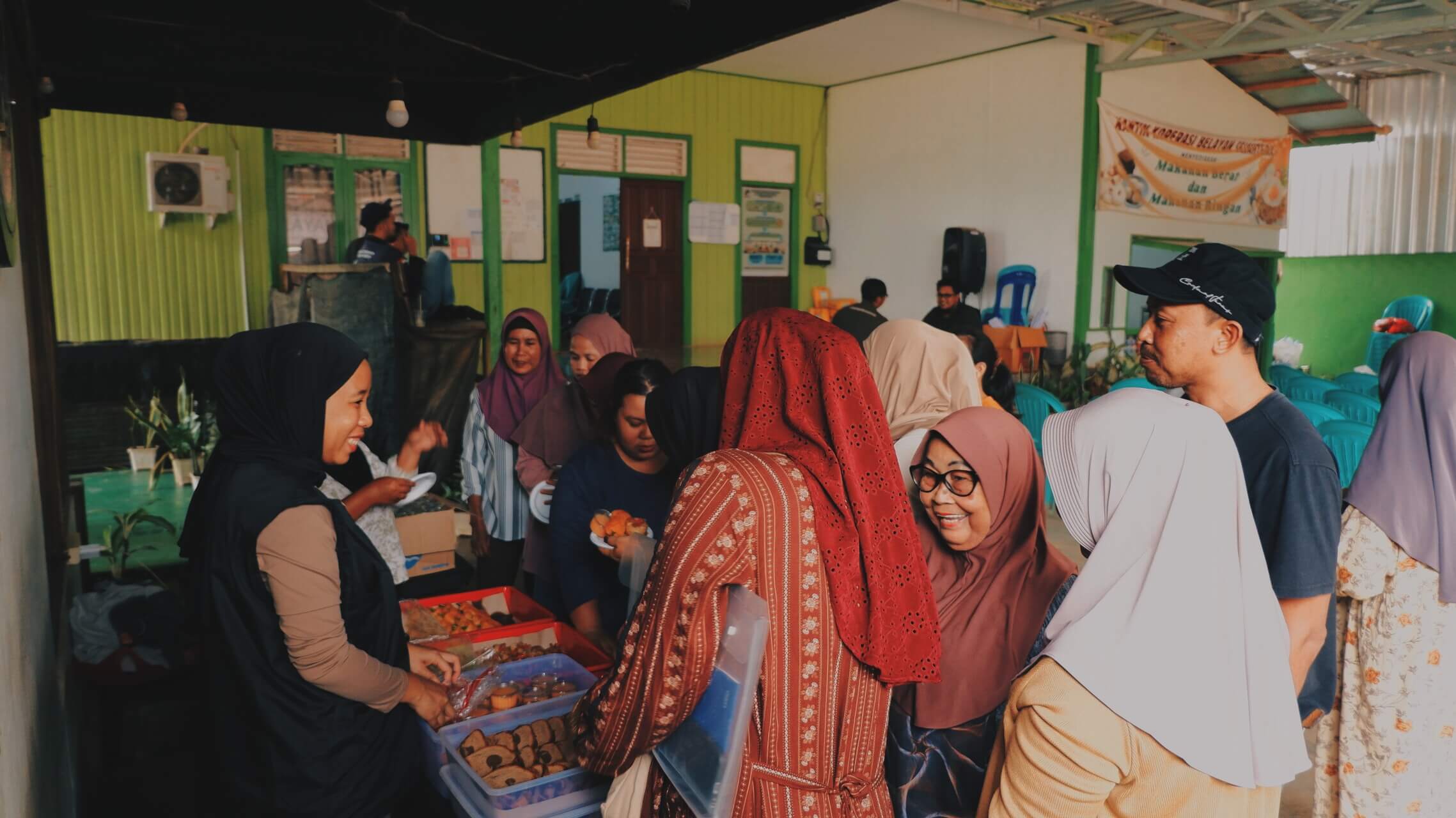 Community members gather indoors around tables of food and local products.